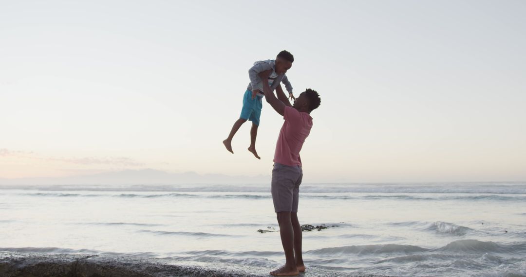 African american father carrying his son on sunny beach - Free Images, Stock Photos and Pictures on Pikwizard.com