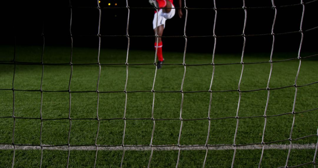 Soccer player kicking ball towards goal during night match - Free Images, Stock Photos and Pictures on Pikwizard.com