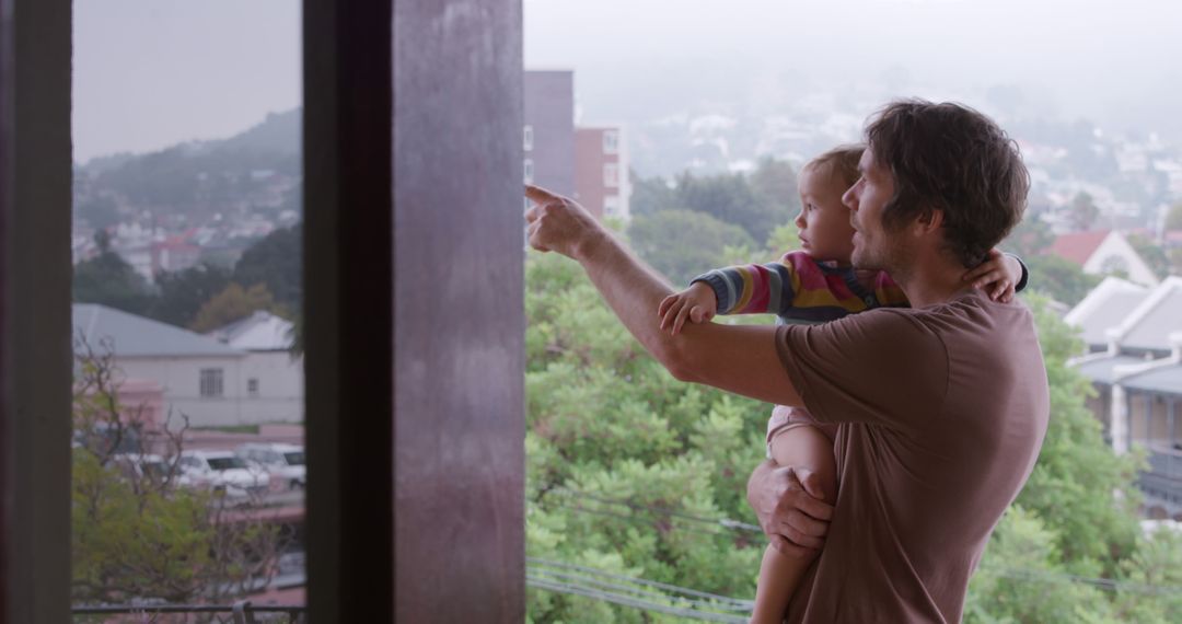 Father Holding Child Pointing Out Window in City Apartment - Free Images, Stock Photos and Pictures on Pikwizard.com