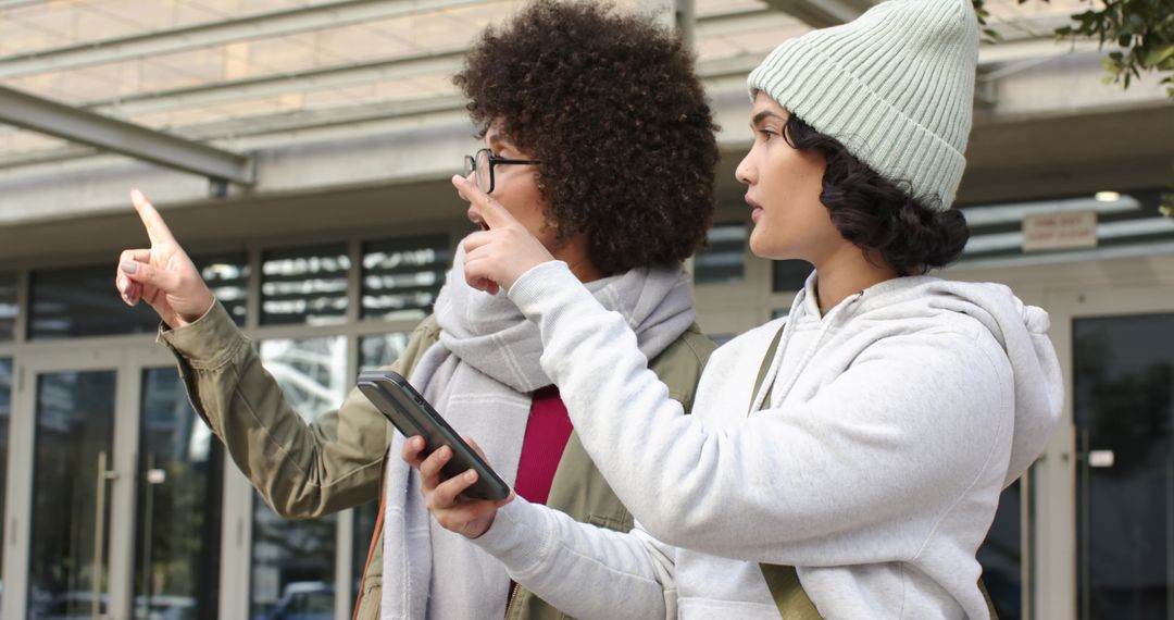 Young women navigating urban entrance using smartphone while pointing toward building