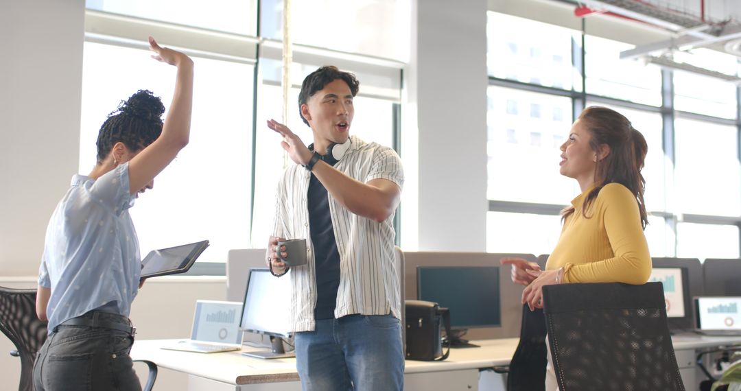 Multicultural team collaborating and celebrating in modern sunlit open-plan office