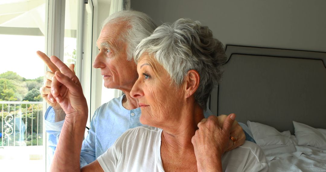 Senior couple looking out window and pointing, enjoying view in bright room - Free Images, Stock Photos and Pictures on Pikwizard.com