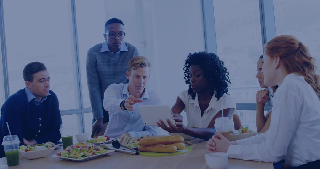 Multicultural team collaborating over tablet during working lunch in modern office