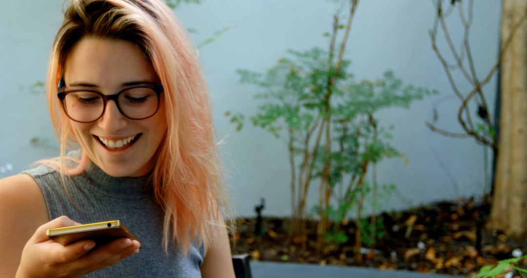 Young Woman with Pink Hair Smiling While Using a Smartphone Outdoors - Free Images, Stock Photos and Pictures on Pikwizard.com