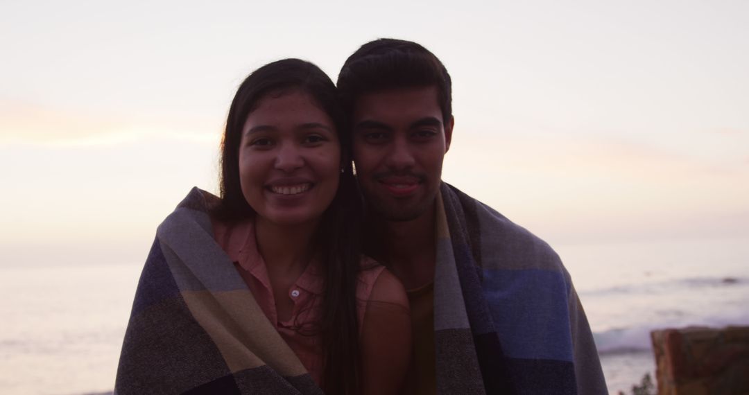 Couple Wrapped in Blanket Smiling Near Beach Sunset - Free Images, Stock Photos and Pictures on Pikwizard.com