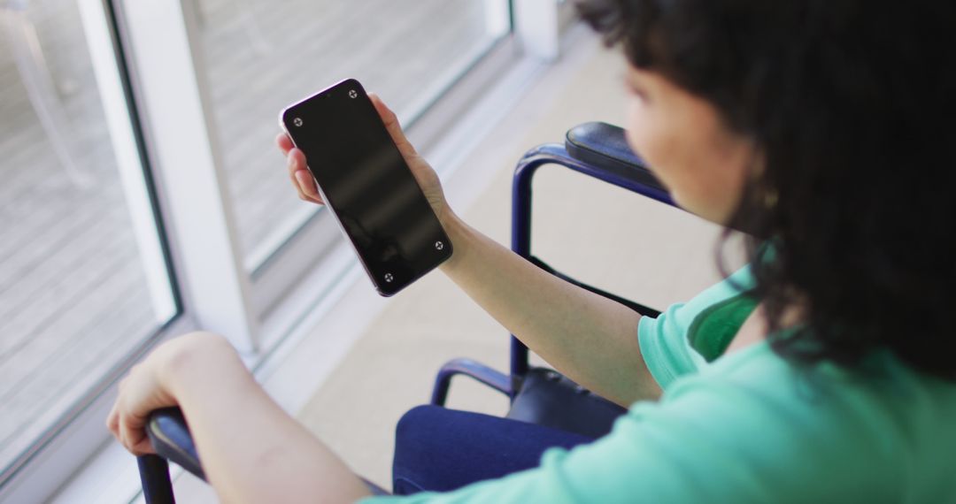 Woman Sitting in Wheelchair Using Smartphone Near Window - Free Images, Stock Photos and Pictures on Pikwizard.com