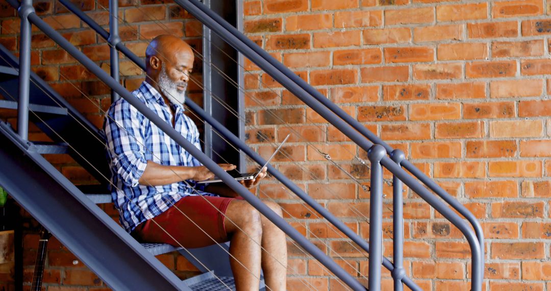 Mature Man Working on Laptop While Sitting on Indoor Staircase - Free Images, Stock Photos and Pictures on Pikwizard.com