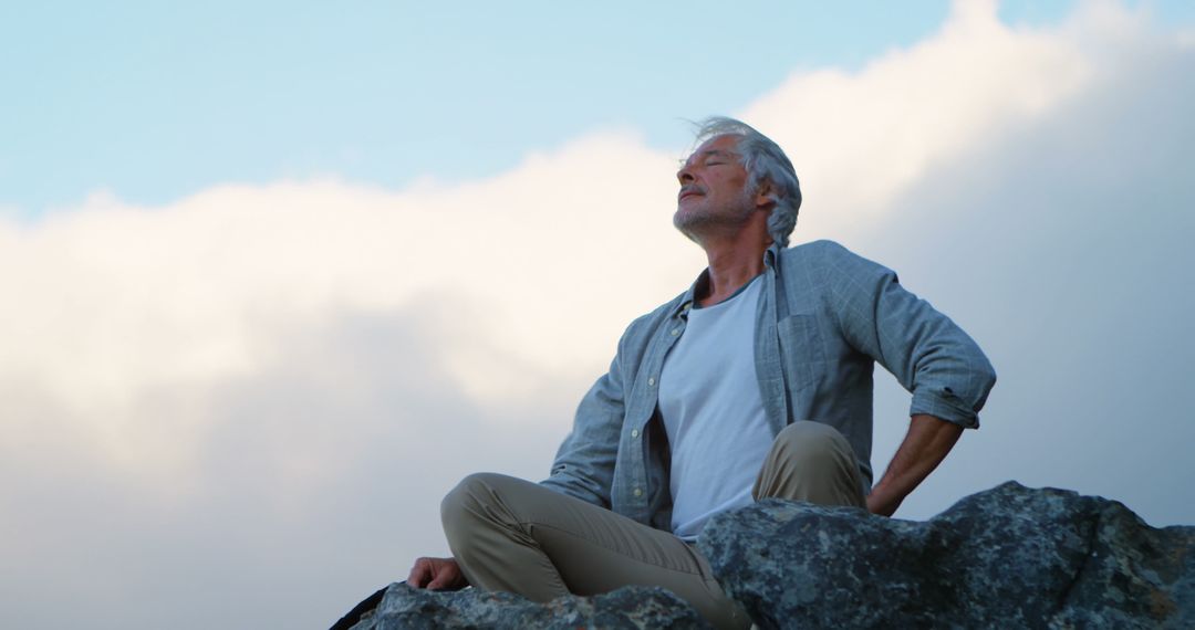 Serene Senior Man Meditating Outdoors Against Cloudy Skies - Free Images, Stock Photos and Pictures on Pikwizard.com