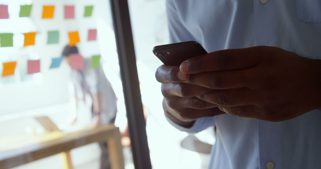 Hands Holding Smartphone in Modern Office with Colleagues in Background - Free Images, Stock Photos and Pictures on Pikwizard.com