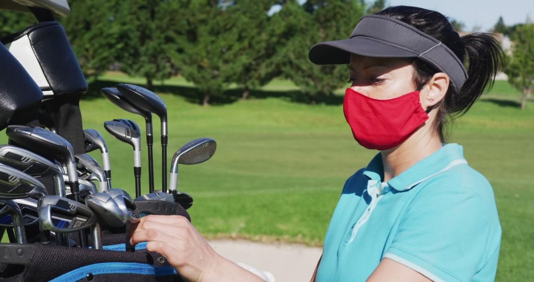 Caucasian woman playing golf wearing face masks taking a golf club from ...