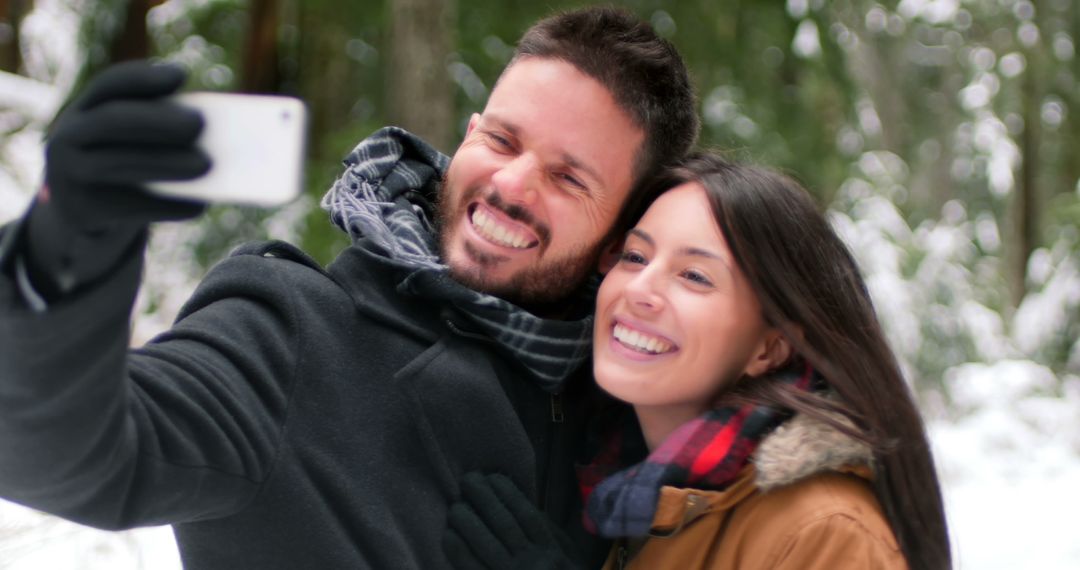 Smiling Couple Taking Selfie in Snowy Forest While Wearing Winter Clothing - Free Images, Stock Photos and Pictures on Pikwizard.com