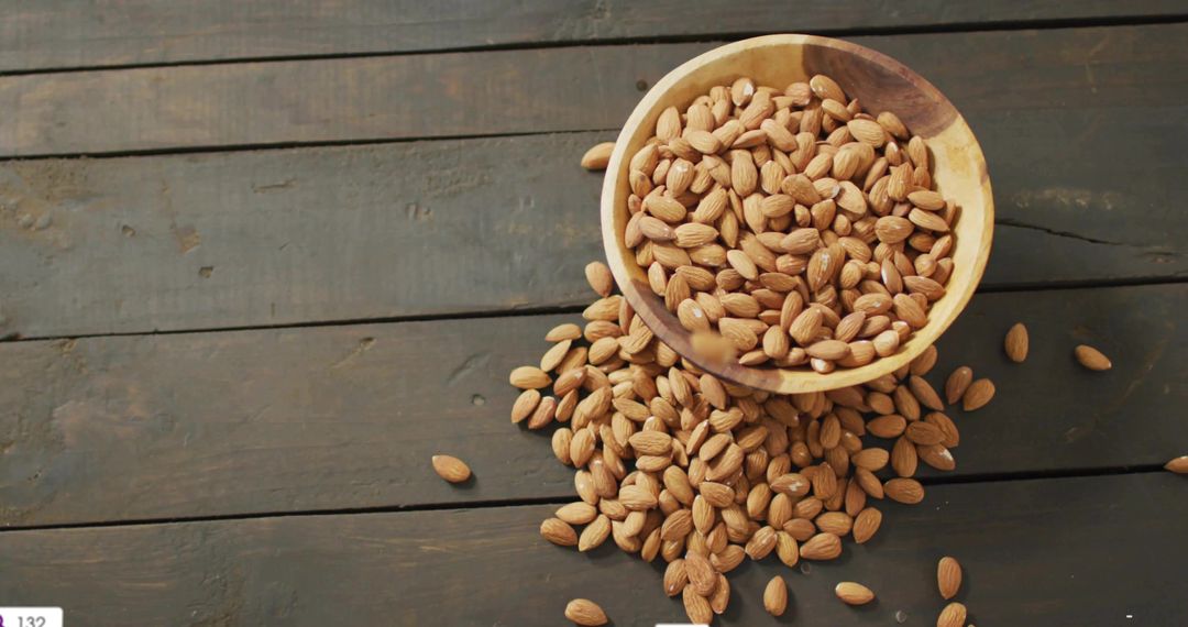 Shelled Almonds Spilling from Wooden Bowl on Rustic Table