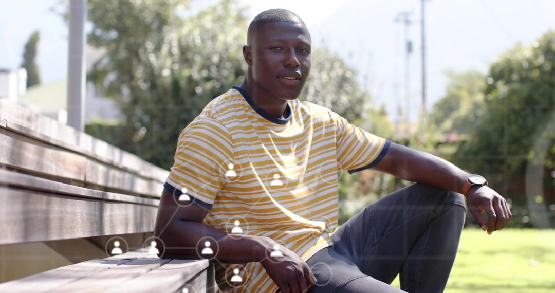 Young man sitting on bench checking watch with social network overlay in sunlit park