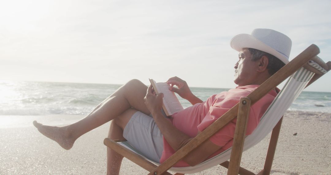 Hispanic Senior Man Relaxing on Beach Reading Book at Sunset
