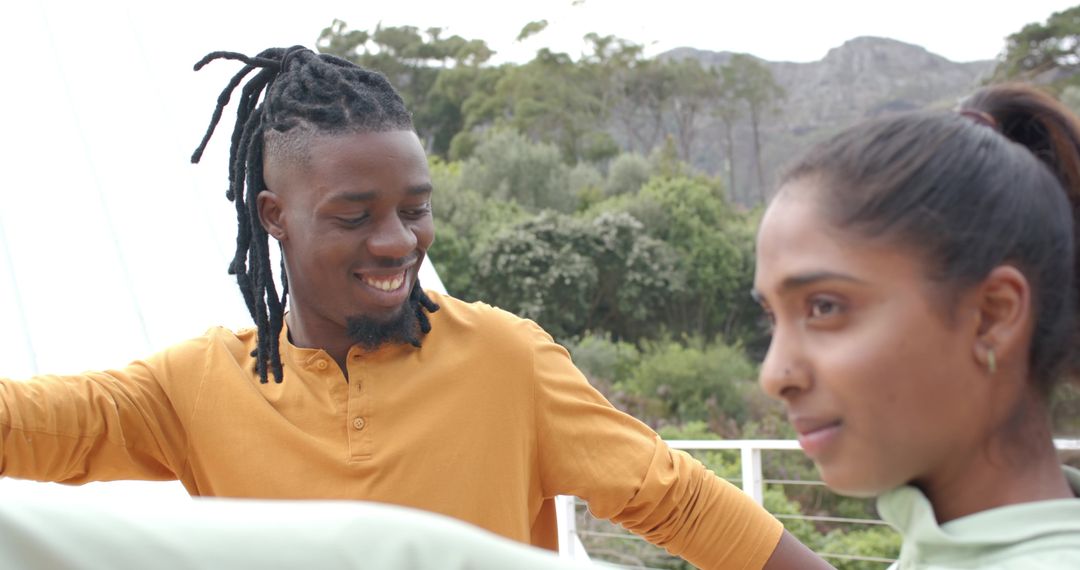 Smiling Black man and South Asian woman leaning on balcony railing enjoying mountain view