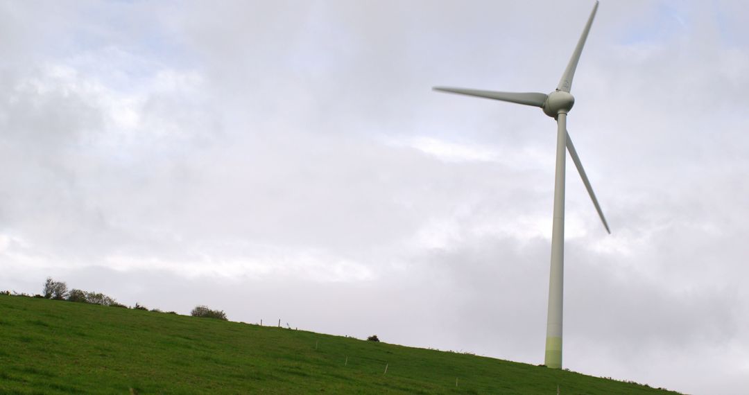 Wind Turbine on Green Hillside Under Cloudy Sky for Renewable Energy - Free Images, Stock Photos and Pictures on Pikwizard.com