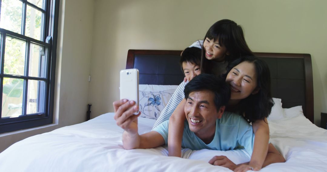 Asian Family Smiling While Taking Selfie on Bed at Home