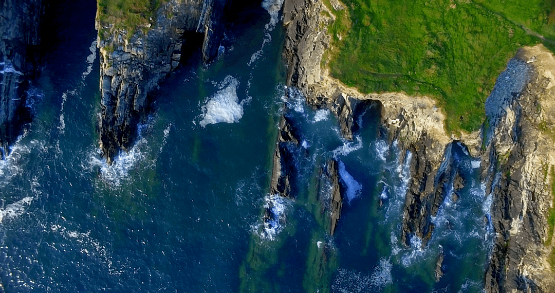Transparent Waves Crashing Against Steep Cliffs from Aerial View