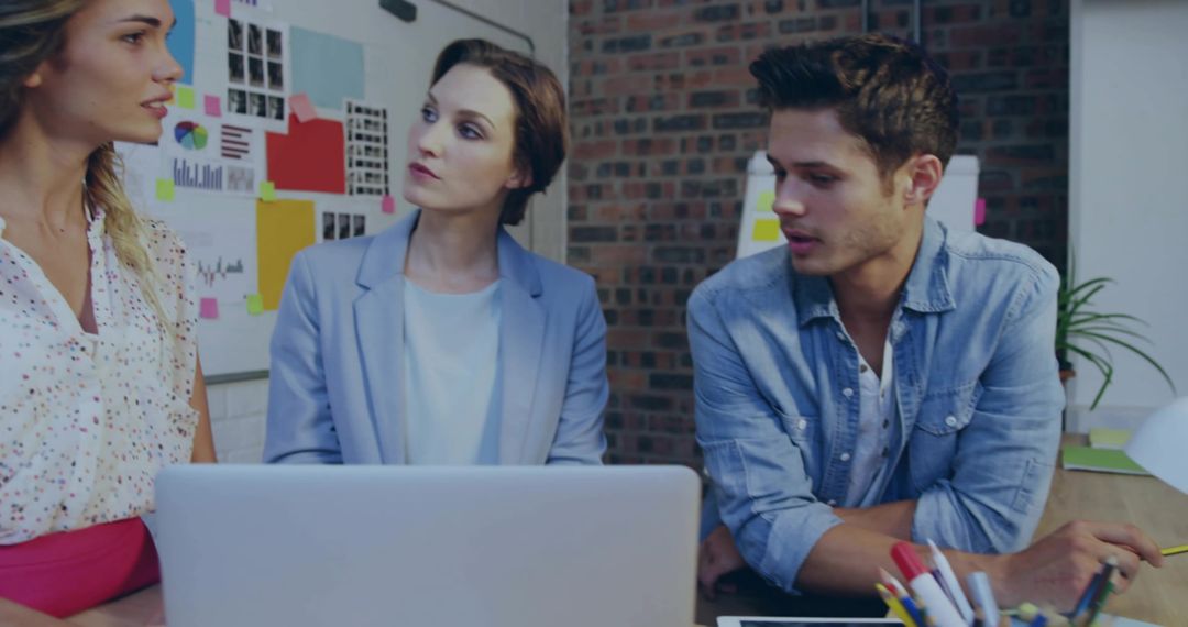 Creative startup team brainstorming around laptop with charts on board in modern office