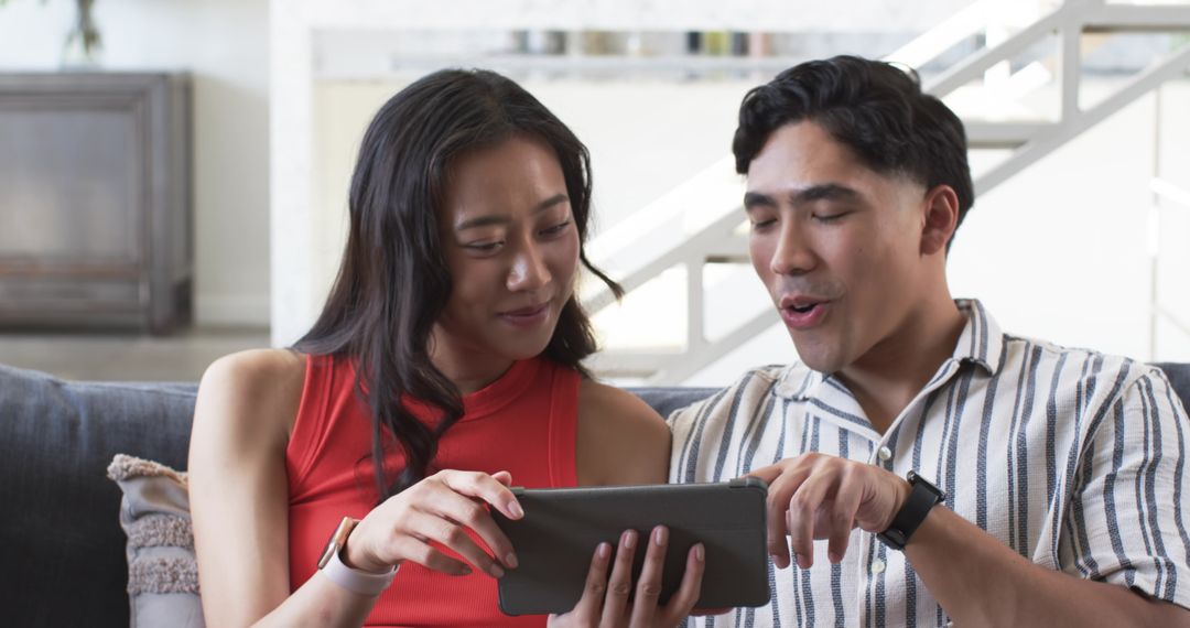 Couple using tablet on sofa sharing content and laughing together