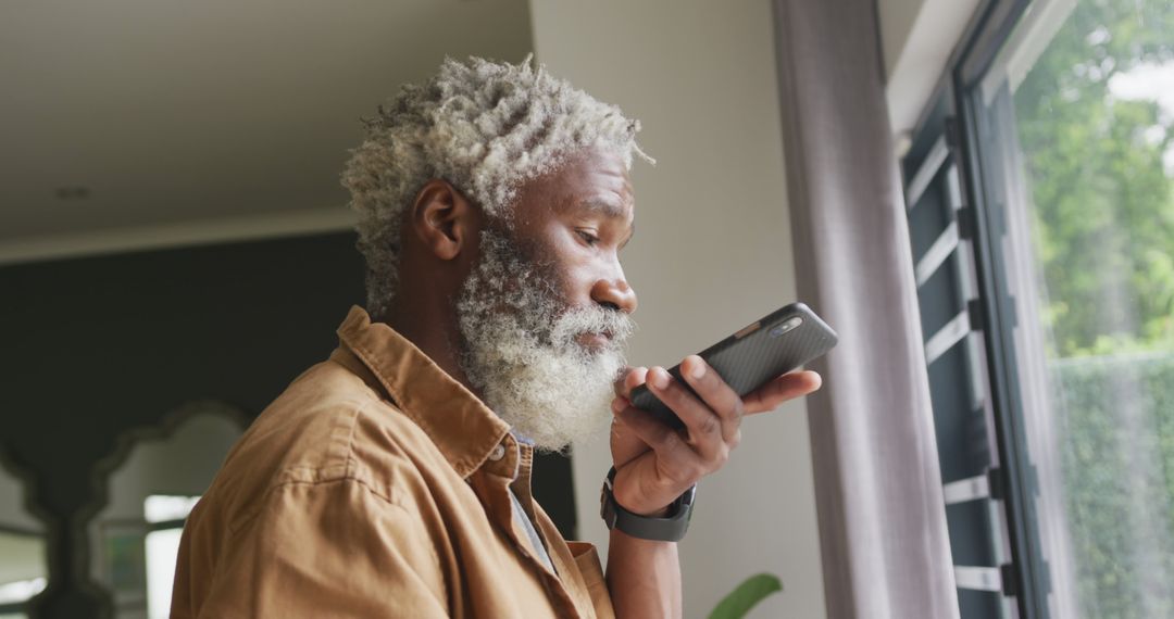 Elderly Man Using Voice Command on Smartphone by Window - Free Images, Stock Photos and Pictures on Pikwizard.com