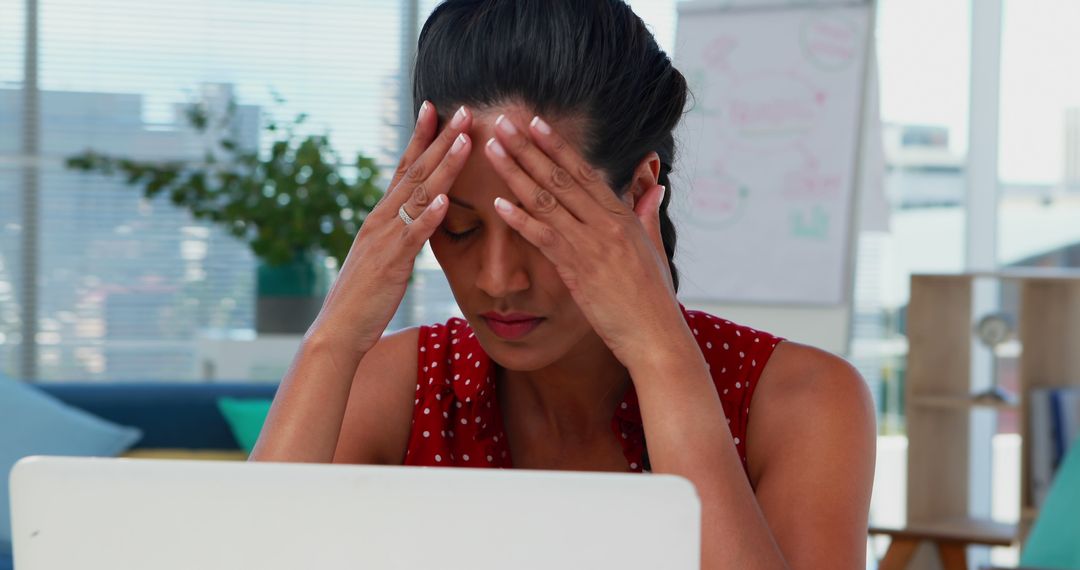 Stressed Businesswoman Holding Head While Working on Laptop in Office - Free Images, Stock Photos and Pictures on Pikwizard.com