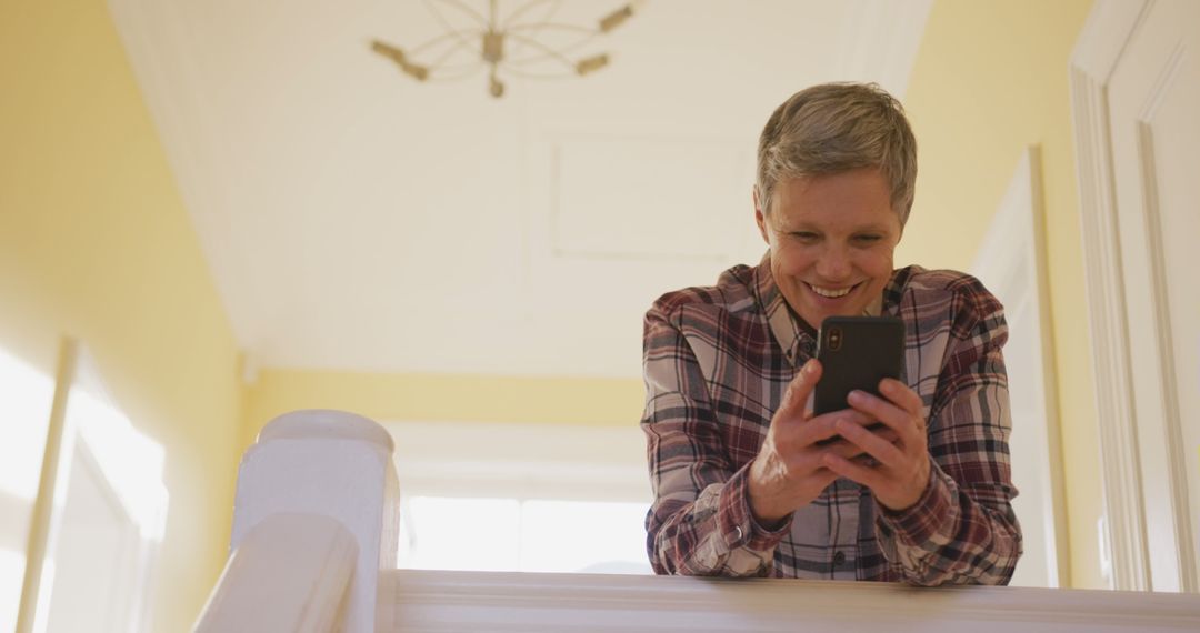 Mature woman laughing while texting on smartphone in bright home - Free Images, Stock Photos and Pictures on Pikwizard.com