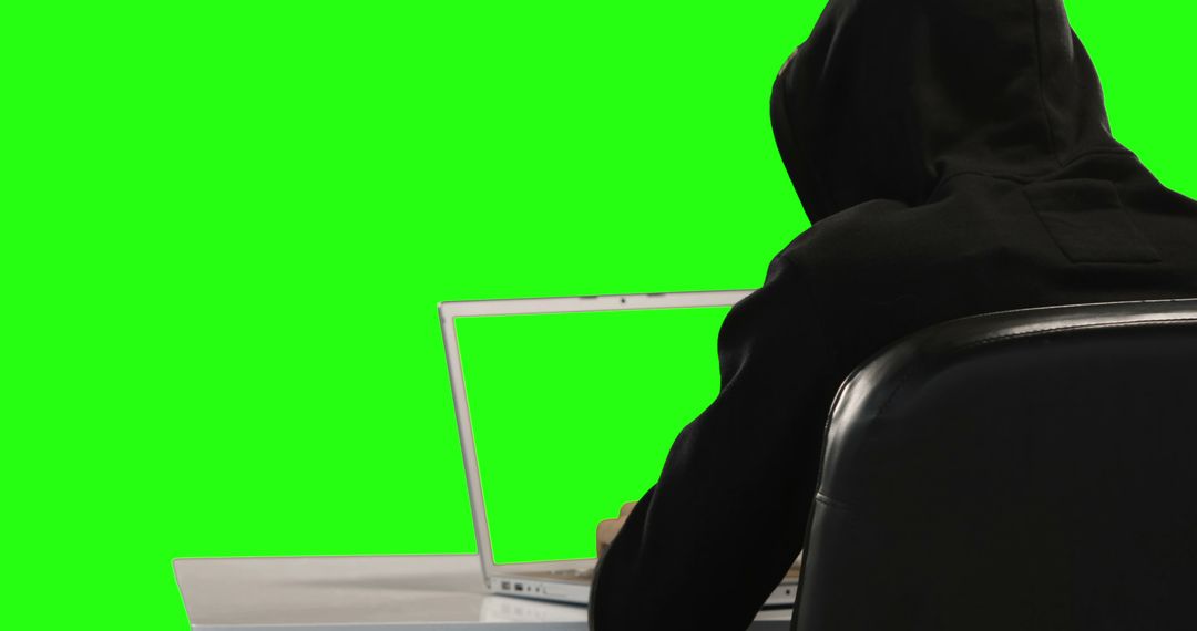 A person in a black hoodie is using a laptop against a green screen background, with copy space - Free Images, Stock Photos and Pictures on Pikwizard.com