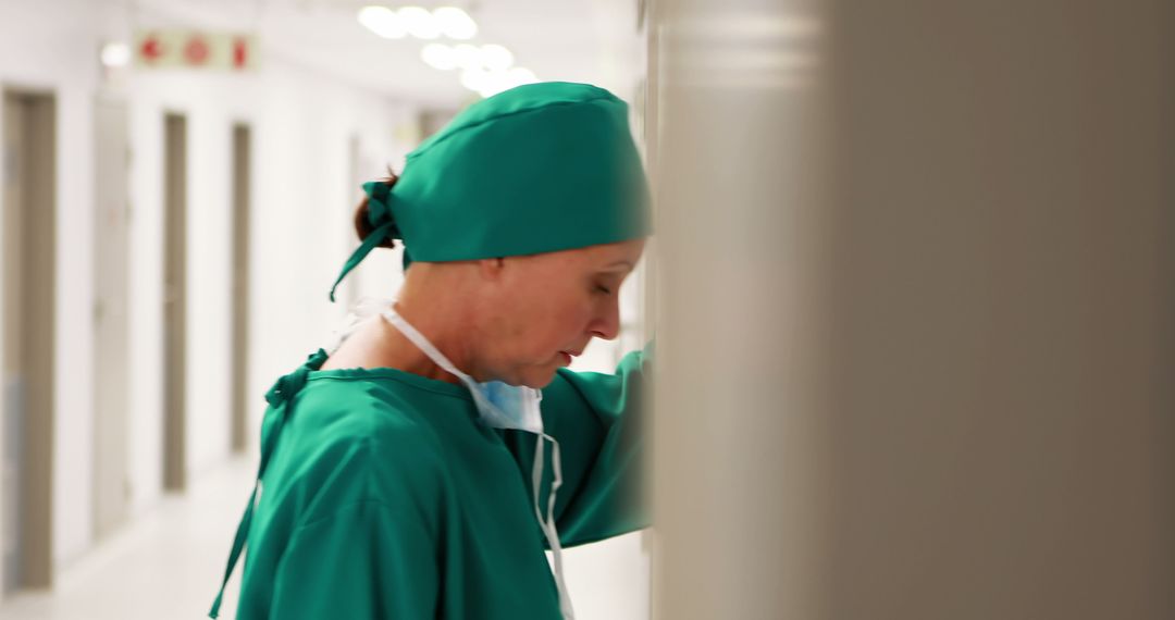 Stressed Female Surgeon Leaning Against Wall in Hospital Corridor - Free Images, Stock Photos and Pictures on Pikwizard.com