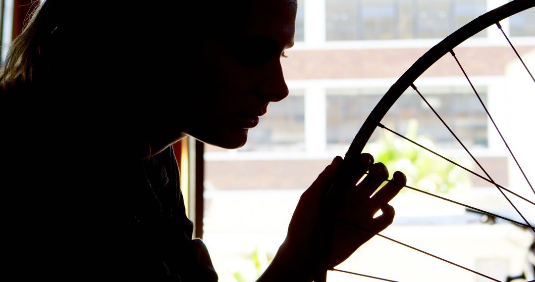 Silhouette of Woman Holding Bicycle Wheel Indoors - Free Images, Stock Photos and Pictures on Pikwizard.com