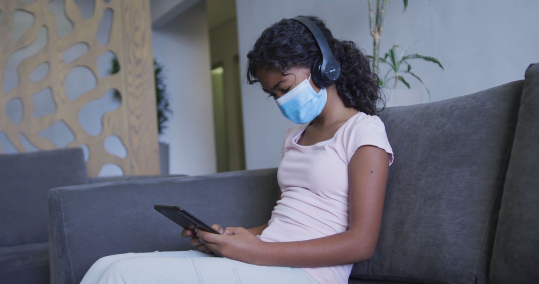 Girl Using Tablet with Mask and Headphones in Hospital Lounge - Free Images, Stock Photos and Pictures on Pikwizard.com