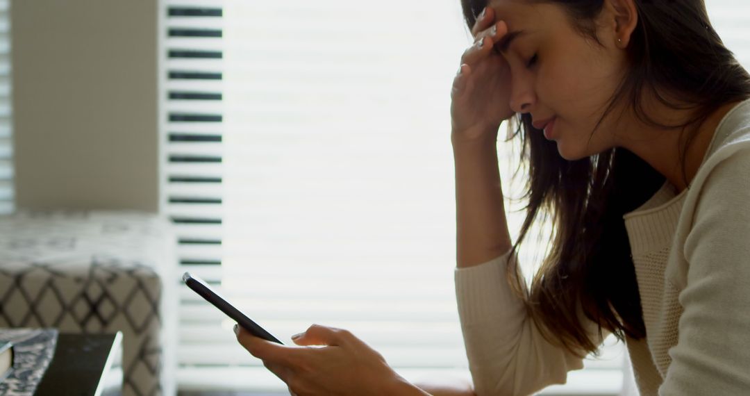 Stressed Woman Looking at Smartphone While Seated Indoors - Free Images, Stock Photos and Pictures on Pikwizard.com