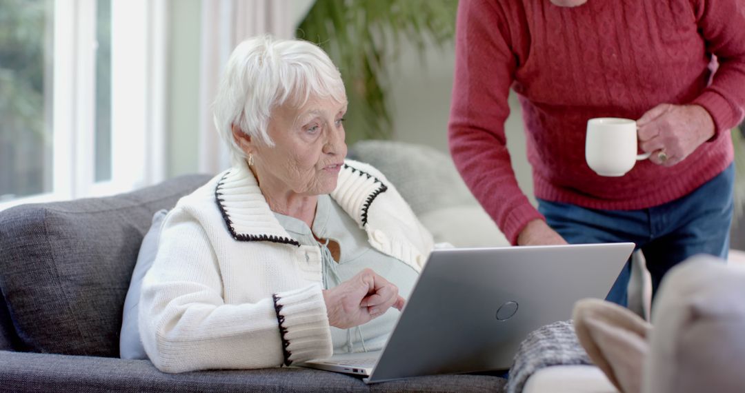 Older Woman Using Laptop With Help of Companion Holding Coffee Cup - Free Images, Stock Photos and Pictures on Pikwizard.com