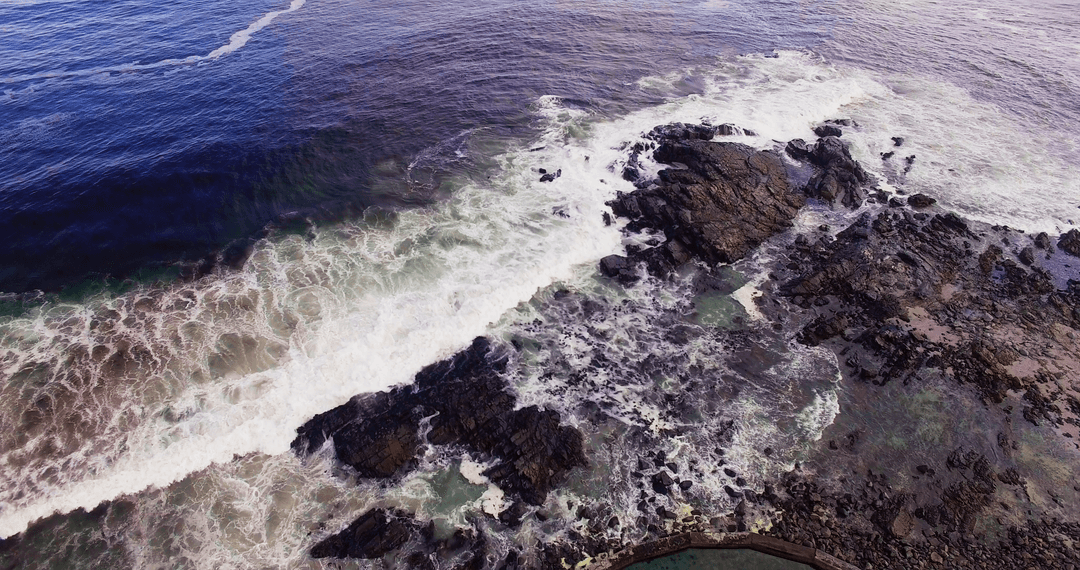 Aerial View of Transparent Waves Crashing on Rocky Shoreline