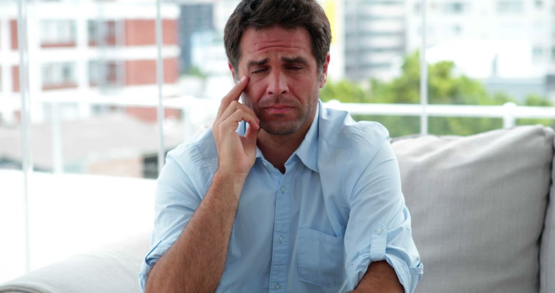 Stressed Man Sitting on Couch Touching Face in City Apartment - Free Images, Stock Photos and Pictures on Pikwizard.com