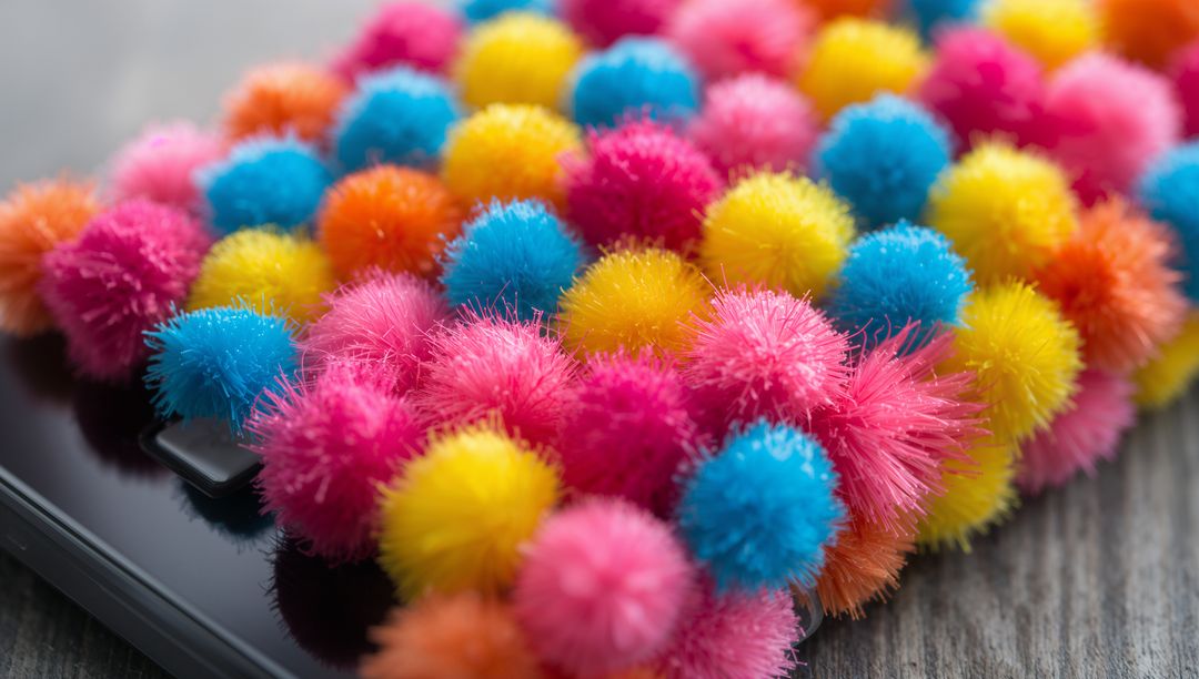 Colorful fuzzy pom-pom cluster covering glossy smartphone macro closeup with bokeh texture