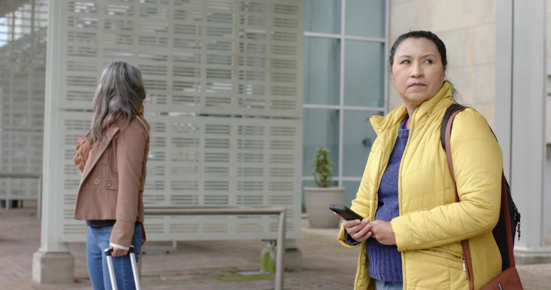 Commuters waiting at transit hub woman in yellow jacket holding smartphone looking away