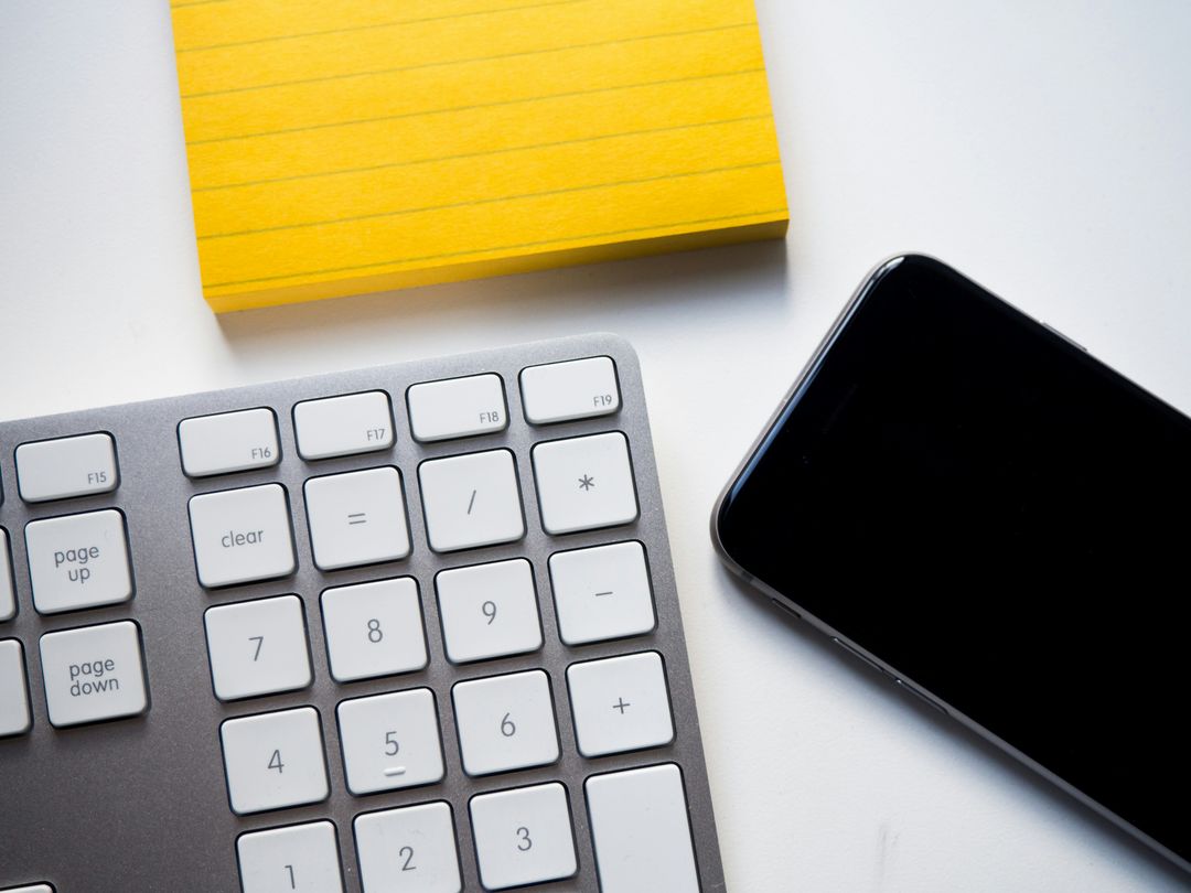 Technology workspace: smartphone, keyboard, yellow notepad