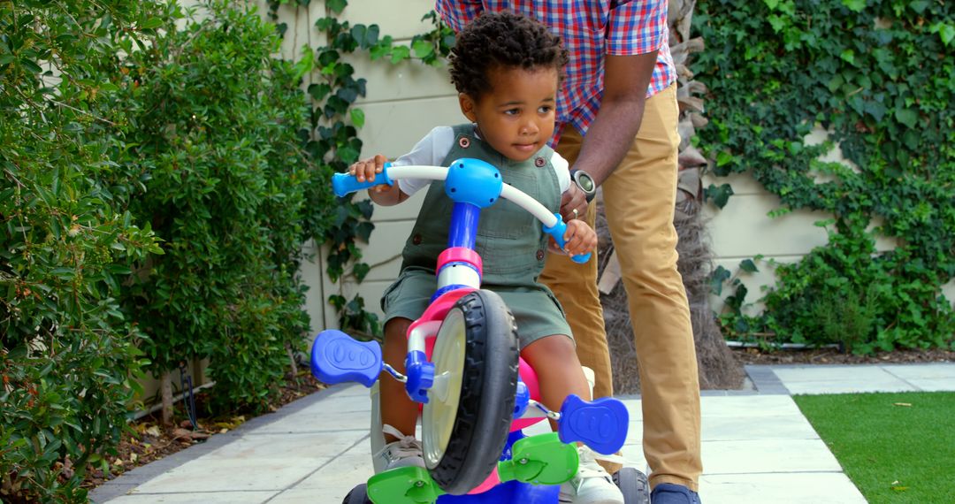 Father Helping Child Ride Toy Tricycle Outdoors - Free Images, Stock Photos and Pictures on Pikwizard.com