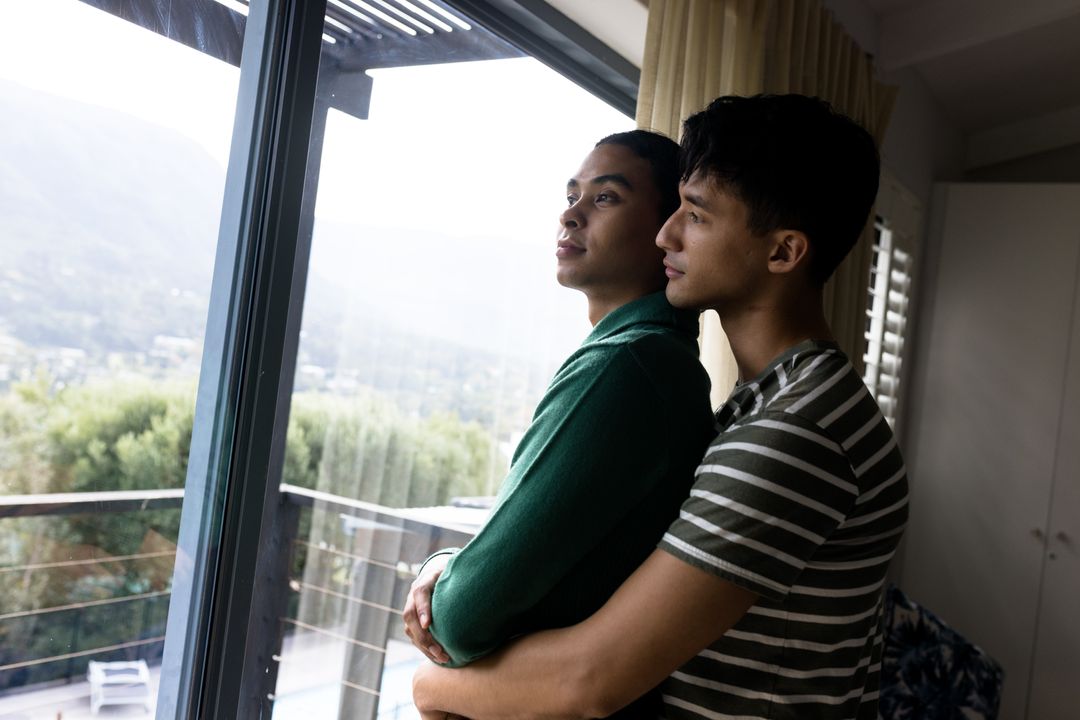 Romantic multiracial gay couple embracing and looking through window at home, copy space - Free Images, Stock Photos and Pictures on Pikwizard.com