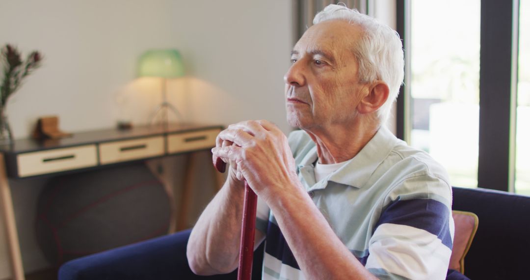 Elderly man reflecting at home with cane - Free Images, Stock Photos and Pictures on Pikwizard.com