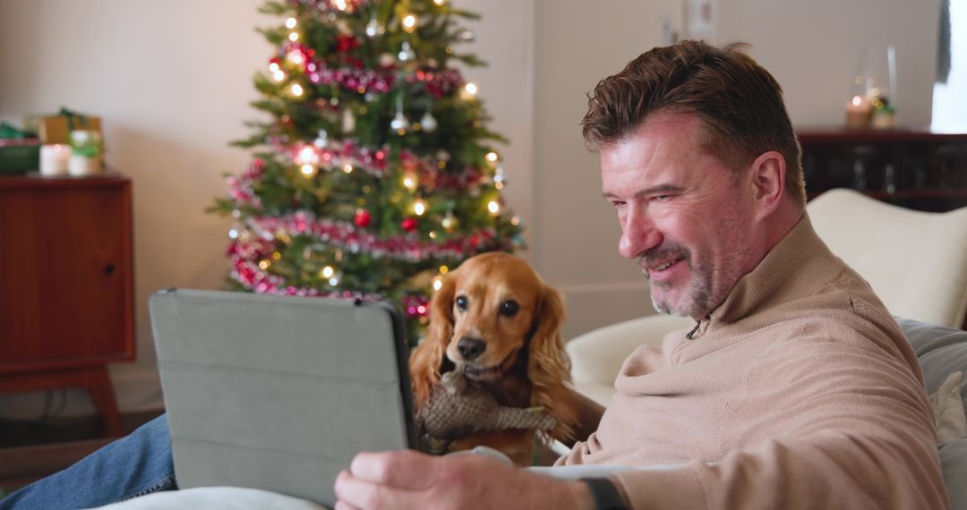 Smiling Man and Relaxed Spaniel Enjoying Tablet Near Christmas Tree