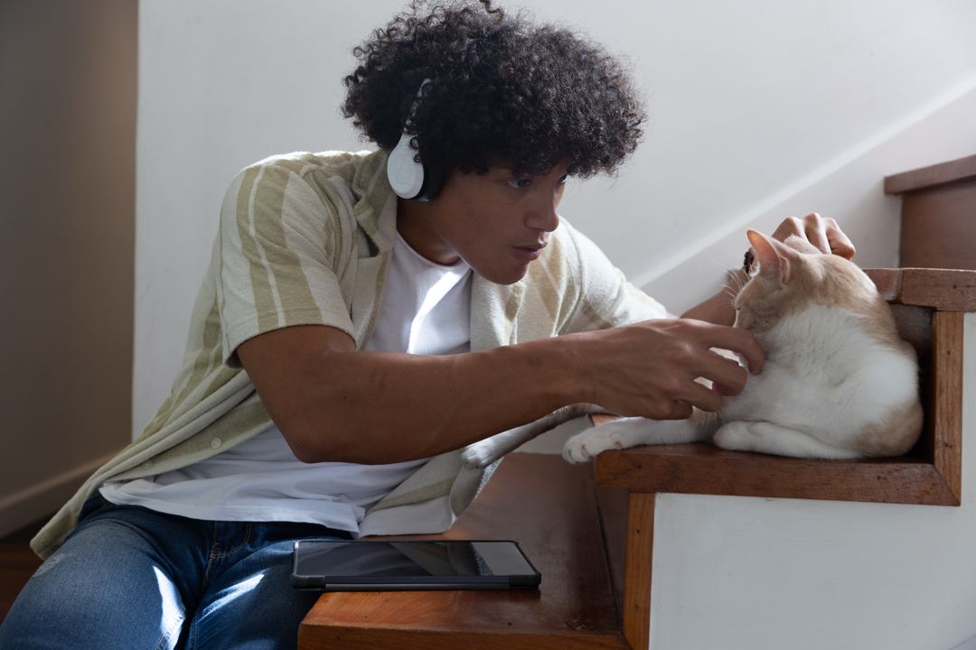 Man with Headphones Bonding with Cat on Staircase at Home
