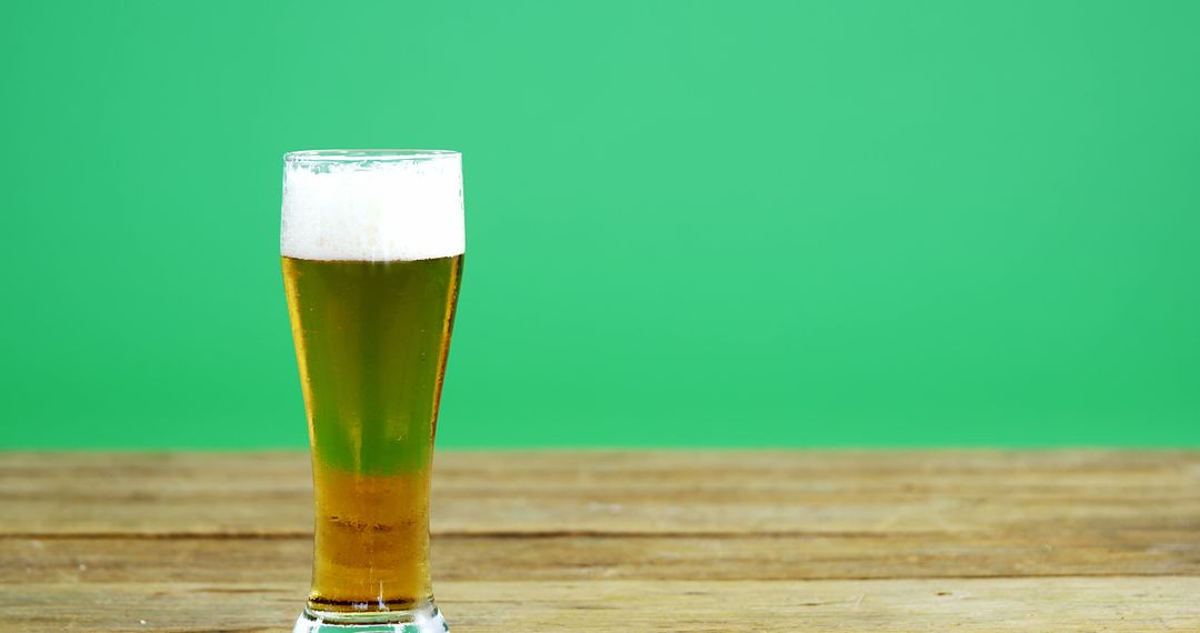 Tall glass of beer with frothy head on wooden table with green background - Free Images, Stock Photos and Pictures on Pikwizard.com