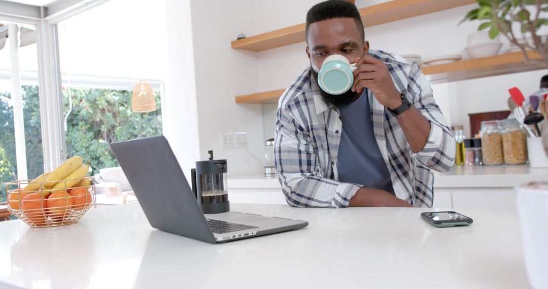 Man Drinking Coffee While Using Laptop in Modern Kitchen - Free Images, Stock Photos and Pictures on Pikwizard.com