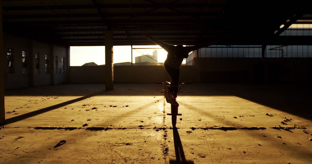 Person Balancing on Bicycle in Abandoned Warehouse at Sunset - Free Images, Stock Photos and Pictures on Pikwizard.com