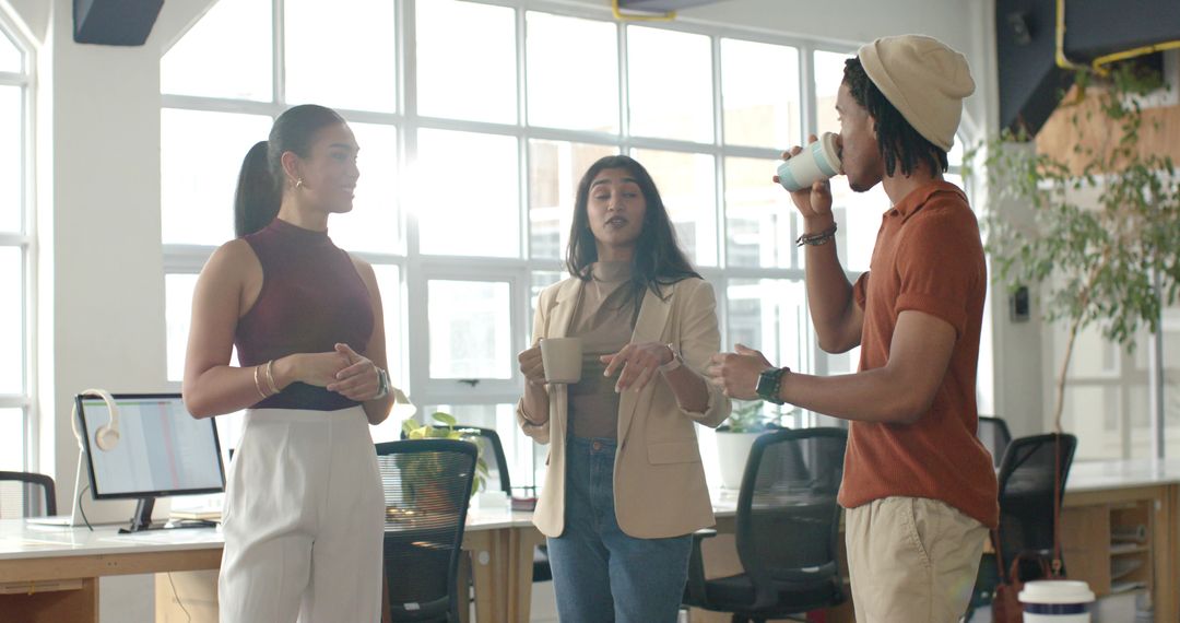 Sunlit modern office team taking coffee break while discussing ideas in open-plan workspace
