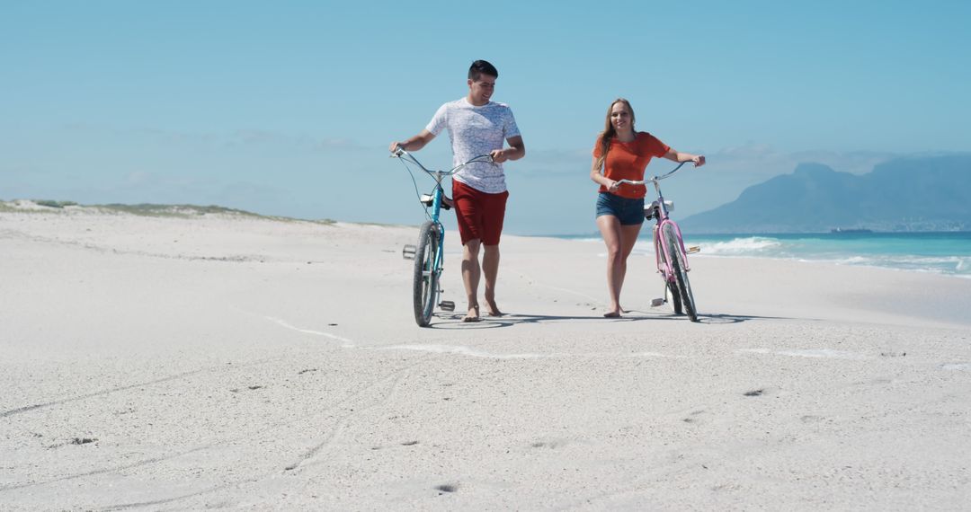 Couple strolling on beach with bicycles, enjoying sunny day - Free Images, Stock Photos and Pictures on Pikwizard.com