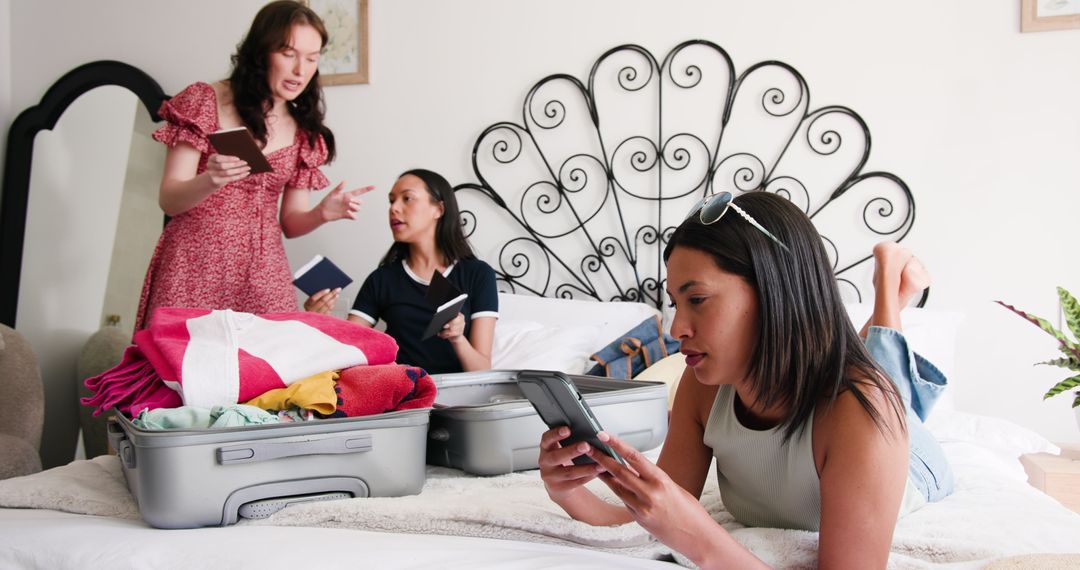 Three Friends Packing for Vacation and Using Smartphones in Bedroom
