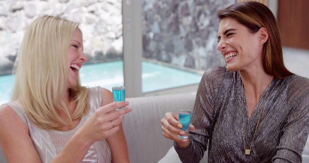 Two Women Laughing and Enjoying Blue Cocktails Together - Free Images, Stock Photos and Pictures on Pikwizard.com